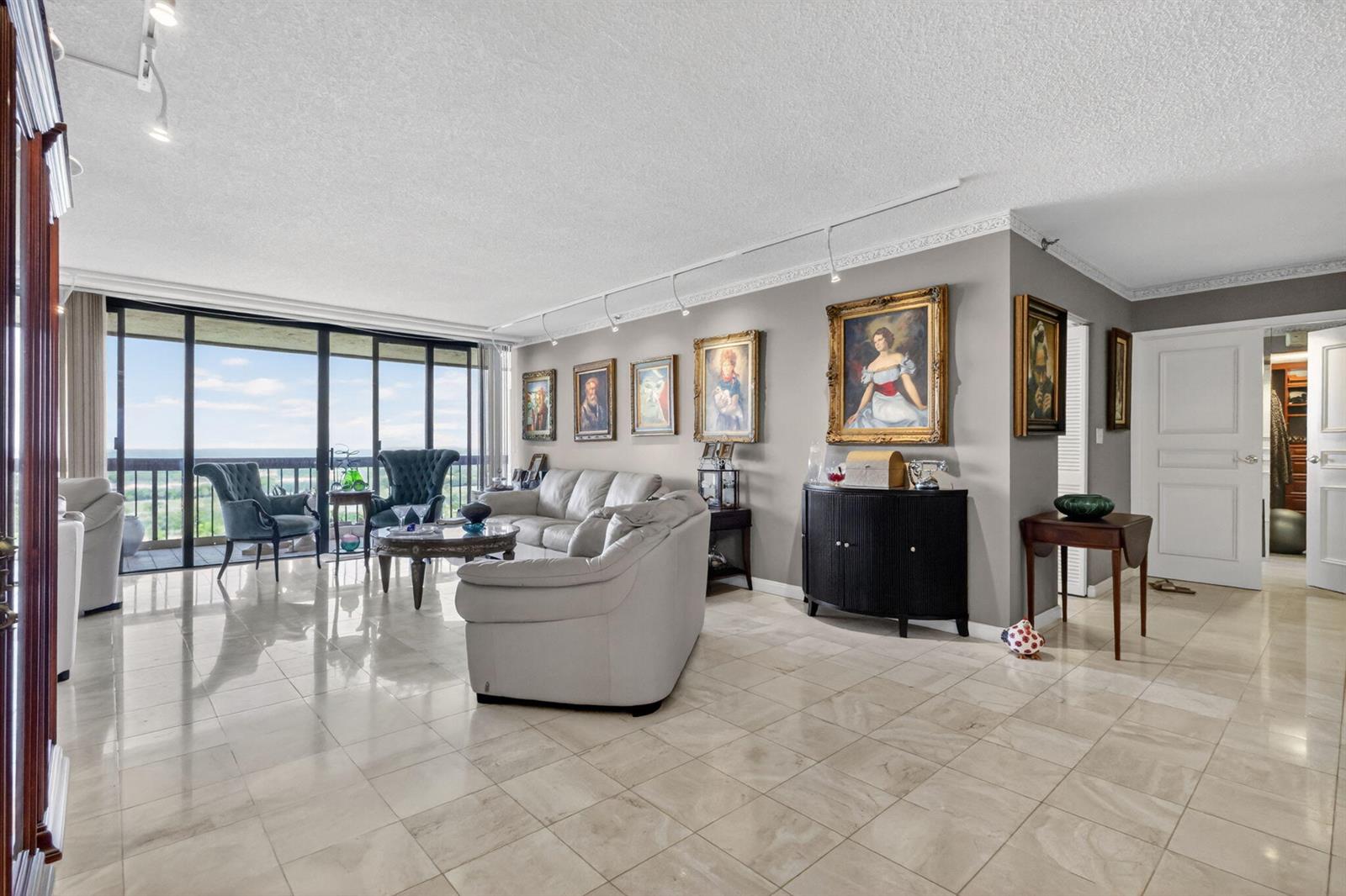 A living room features light tile floors, gray walls, framed portraits, and a balcony view — 1900 Consulate Place # 1705, West Palm Beach FL 33401, WEST PALM BEACH, FL