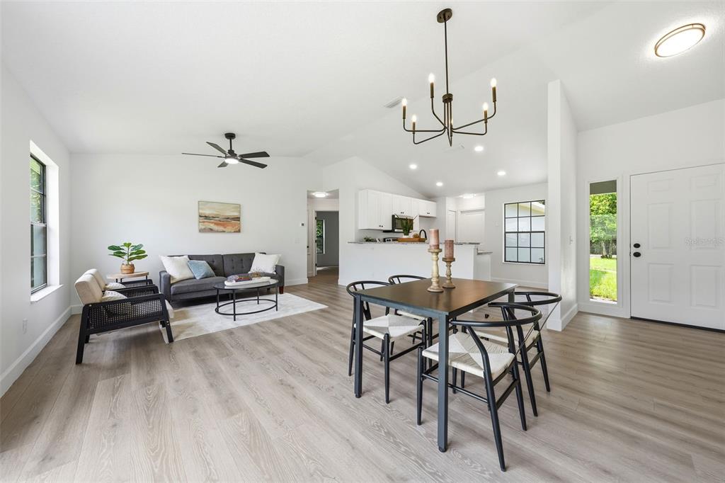 An open-concept living and dining area features light wood-look flooring, white walls, and modern lighting — 350 LAKE CRESCENT DRIVE, DEBARY, FL