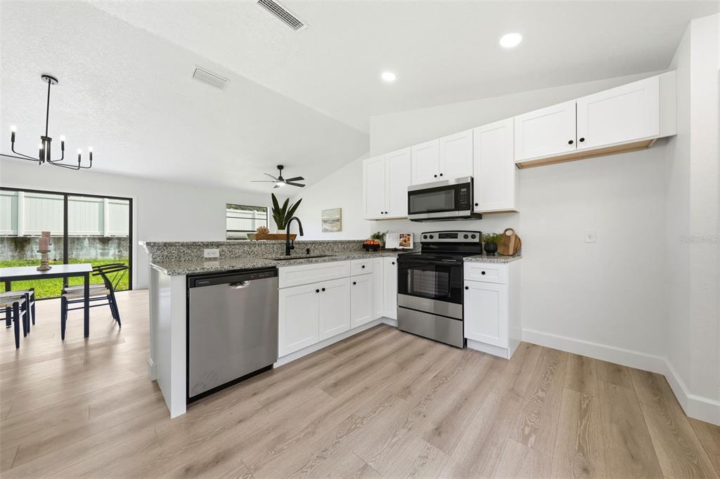 A kitchen with white cabinets, stainless steel appliances, and granite countertops overlooks a dining area — 350 LAKE CRESCENT DRIVE, DEBARY, FL