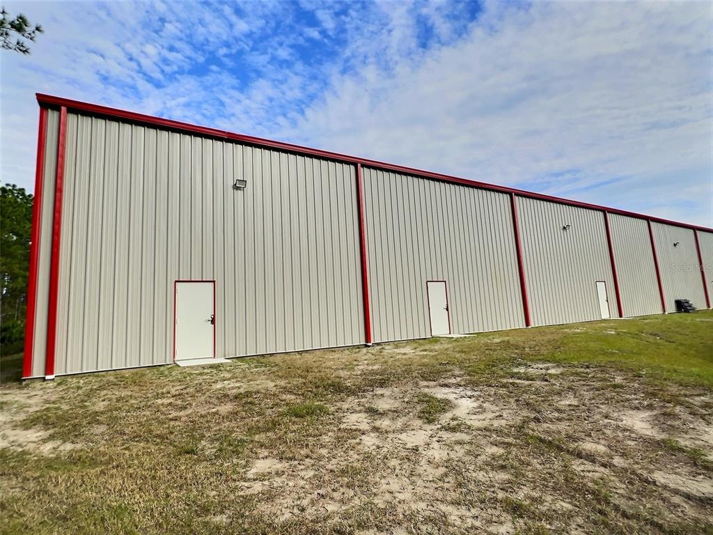 A long, metal-sided industrial building with red trim and three white doors stands outdoors — 25 RAILSIDE WAY UNIT B, PALM COAST, FL