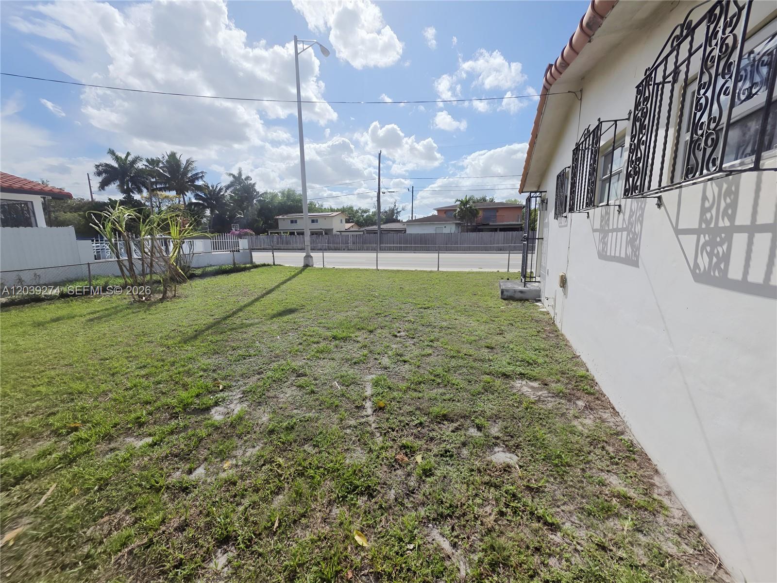 A grassy side yard sits beside a white house with decorative metal window security bars — 405 SE 4th Ave, Hialeah FL 33010, HIALEAH, FL
