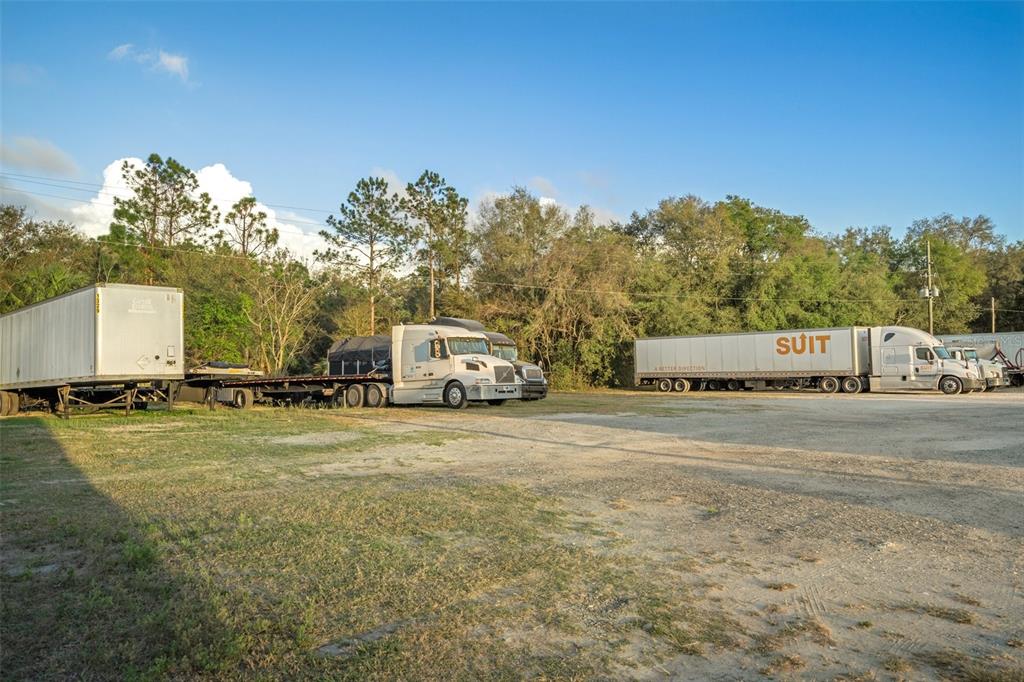 A gravel lot features several semi-trucks and trailers parked in front of a wooded area — 3109 S FLORIDA AVENUE, INVERNESS, FL