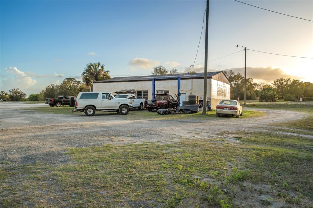 An exterior view of a commercial garage building with several parked vehicles on a dirt lot — 3109 S FLORIDA AVENUE, INVERNESS, FL