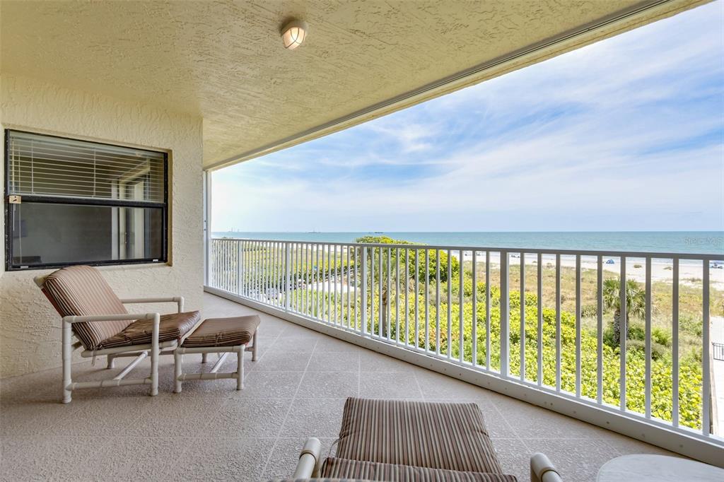 A balcony with a lounge chair and ottoman overlooks a sandy beach and the ocean — 555 HARRISON AVENUE UNIT 402, CAPE CANAVERAL, FL