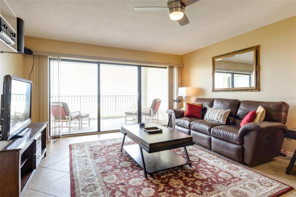 A living room with a brown leather sofa, coffee table, and sliding doors to a balcony — 555 HARRISON AVENUE UNIT 402, CAPE CANAVERAL, FL