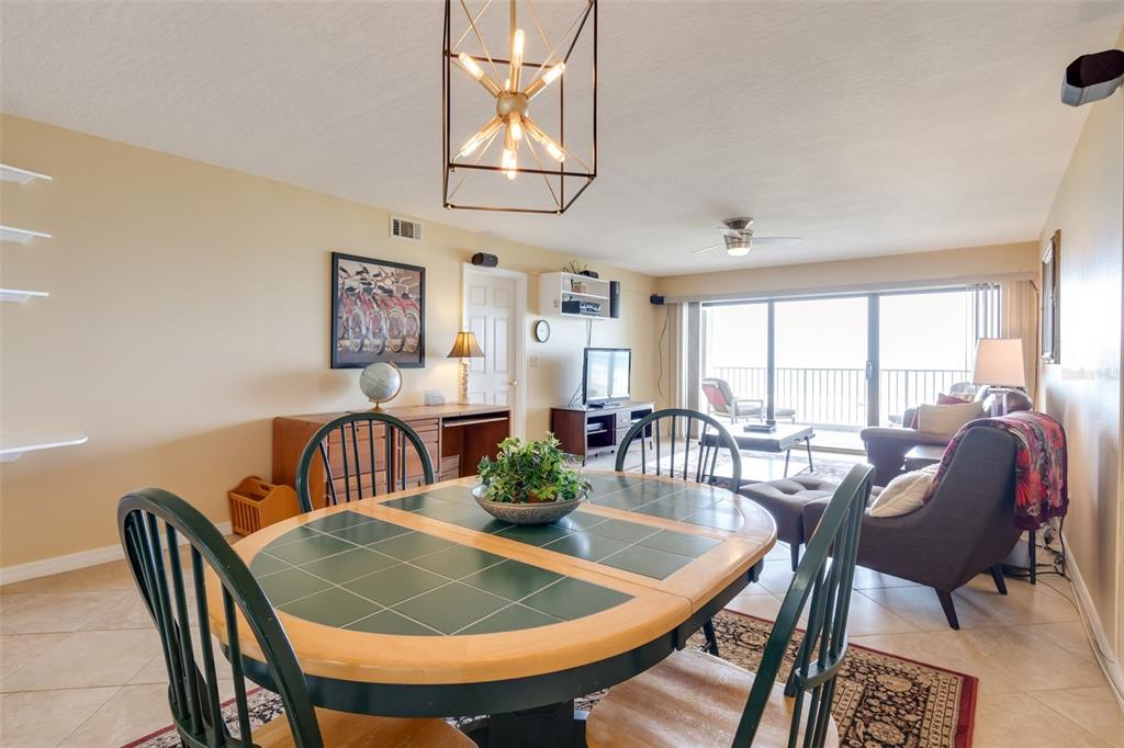 A dining area with a tiled table opens into a living room with balcony access — 555 HARRISON AVENUE UNIT 402, CAPE CANAVERAL, FL