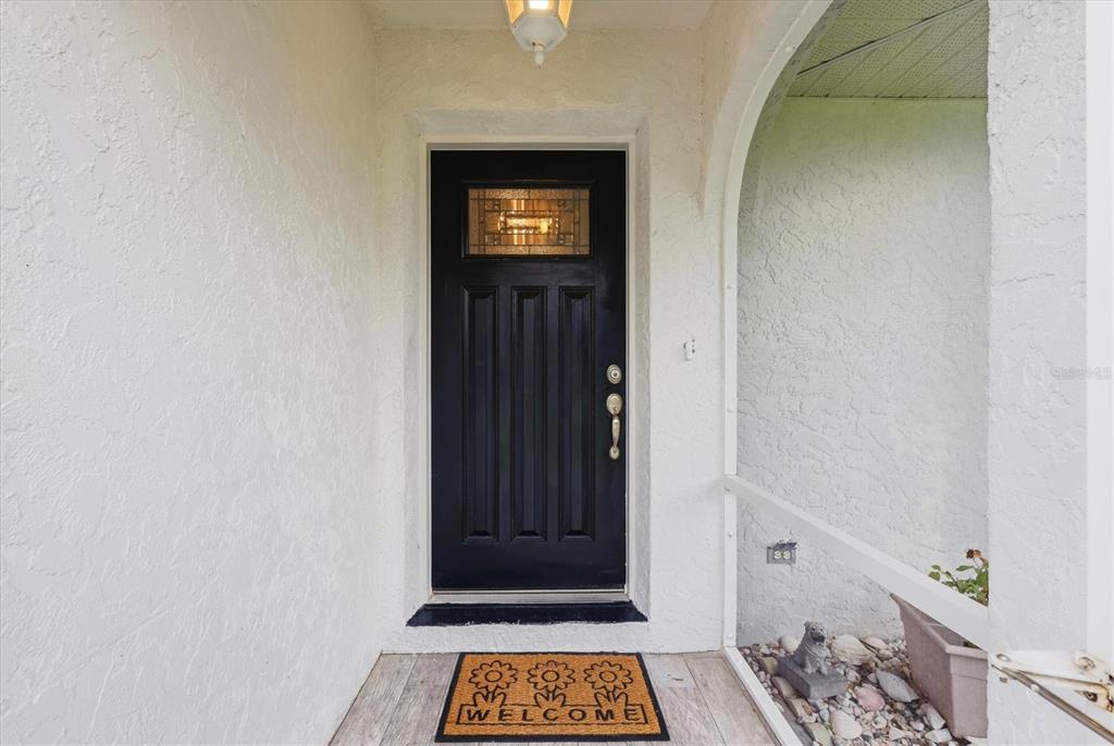 A black front door with a glass insert sits under a covered entryway with stucco walls — 650 CHEVY CHASE STREET, PORT CHARLOTTE, FL