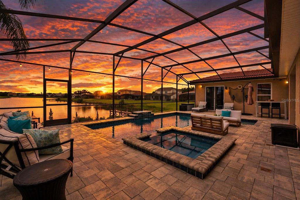 A screened-in patio features a swimming pool, a hot tub, and a sunset lake view — 3704 EAGLE ISLE CIRCLE, KISSIMMEE, FL