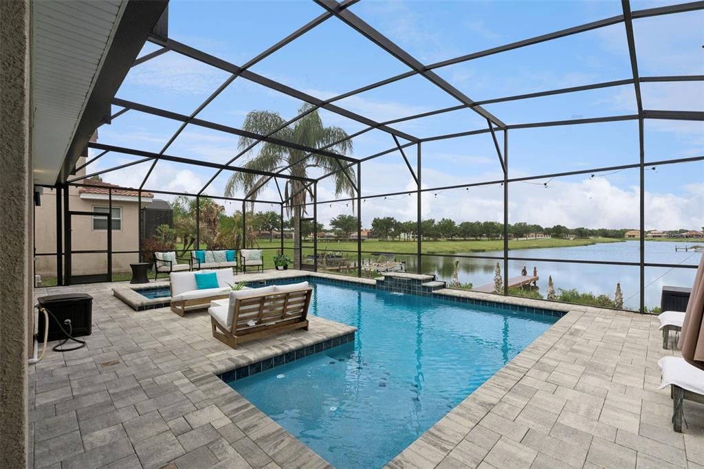 A screened-in patio features a swimming pool, spa, and outdoor seating overlooking a lake — 3704 EAGLE ISLE CIRCLE, KISSIMMEE, FL
