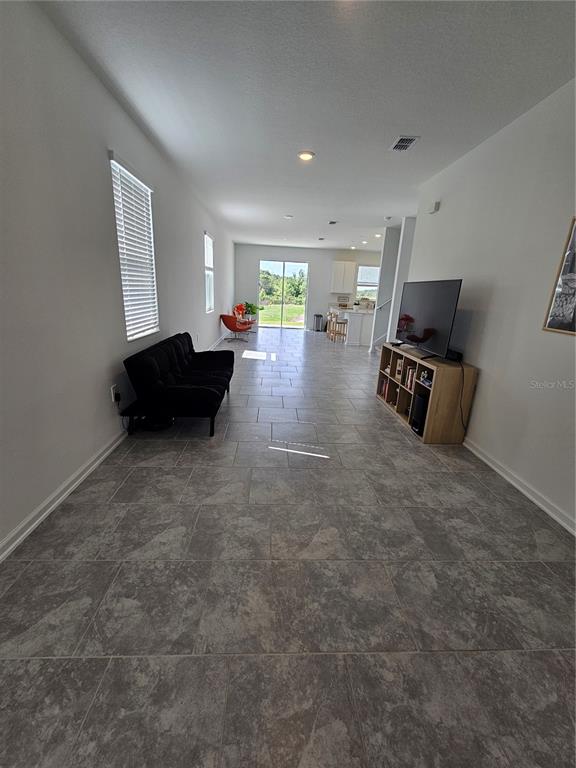 A long, open-concept living area features gray tile flooring, white walls, and a kitchen beyond — 3054 CHANTILLY DRIVE, DAVENPORT, FL