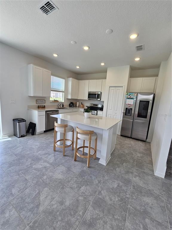 A modern kitchen features white cabinetry, stainless steel appliances, a center island, and tile flooring — 3054 CHANTILLY DRIVE, DAVENPORT, FL