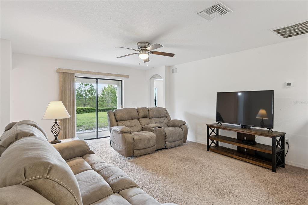 A living room features beige carpet, two reclining sofas, a television stand, and sliding doors — 916 ASPEN VIEW CIRCLE, GROVELAND, FL