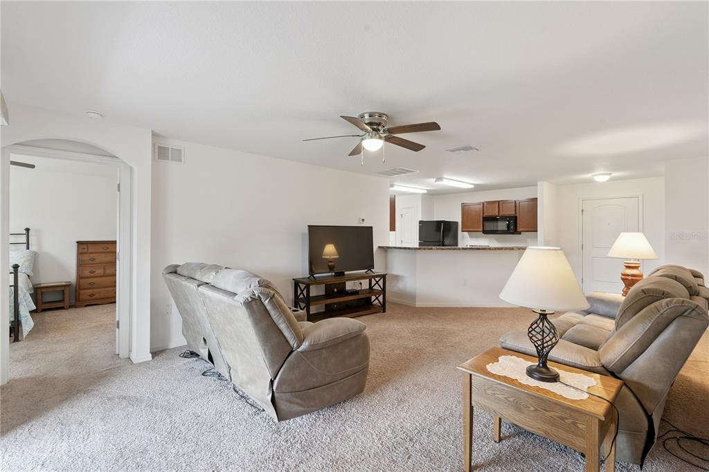 A living room with carpeted floors, a ceiling fan, and an open kitchen in the background — 916 ASPEN VIEW CIRCLE, GROVELAND, FL