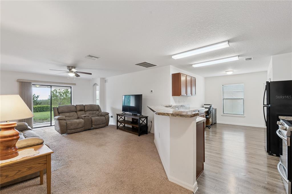 An open-concept living room and kitchen area with carpeted flooring, a breakfast bar, and appliances — 916 ASPEN VIEW CIRCLE, GROVELAND, FL