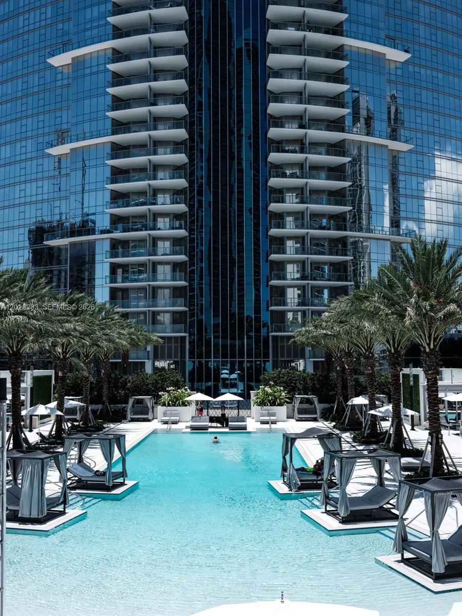 A swimming pool with cabanas sits in front of a modern glass high-rise building — 851 NE 1st Ave # 4107, Miami FL 33132, MIAMI, FL