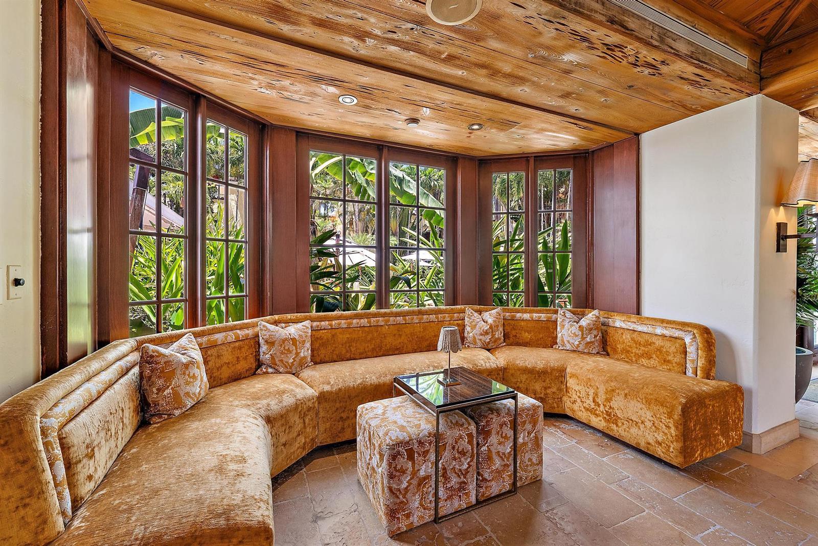 A curved velvet sofa sits in a sunroom with wood-paneled ceilings and large windows — 301 Australian Avenue # 301, Palm Beach FL 33480, PALM BEACH, FL