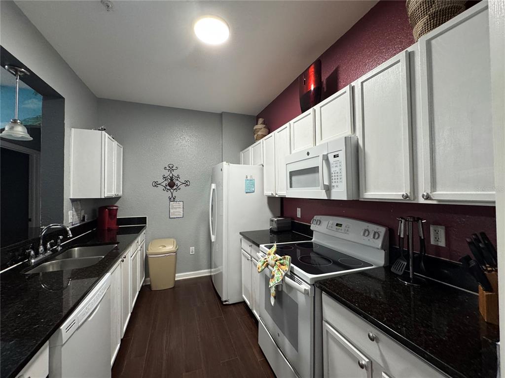 A galley kitchen features white cabinets, black countertops, stainless steel appliances, and dark wood flooring — 2821 ALMATON LOOP UNIT 205, KISSIMMEE, FL