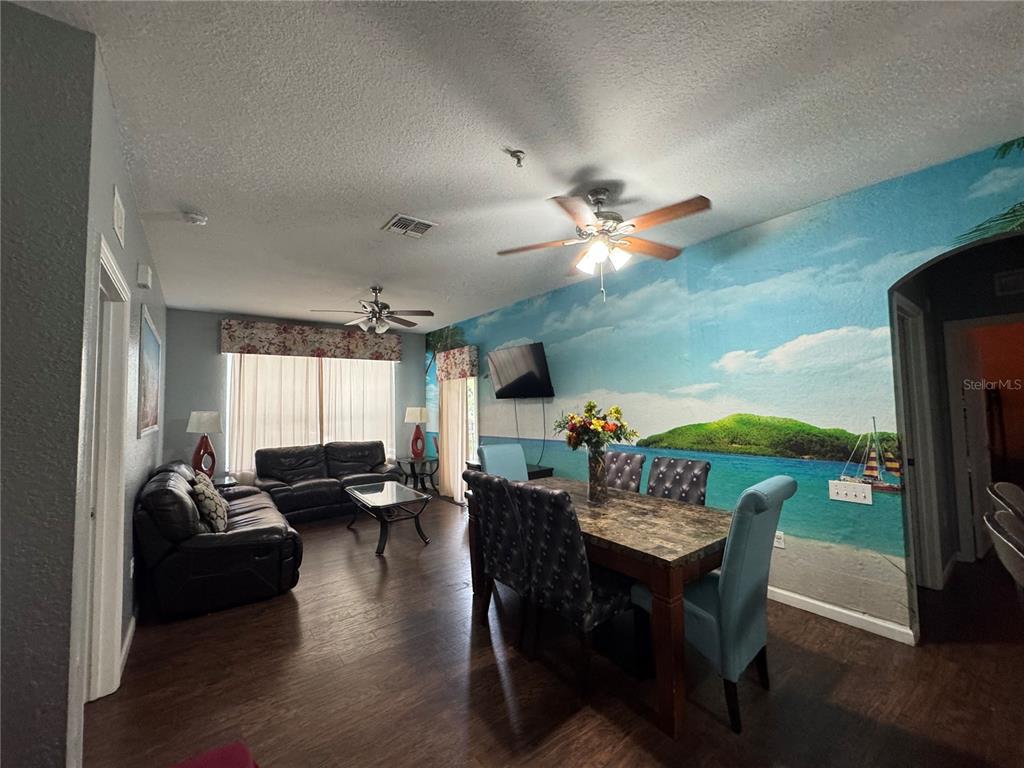 A living and dining area features a large tropical mural, dark leather furniture, and ceiling fans — 2821 ALMATON LOOP UNIT 205, KISSIMMEE, FL