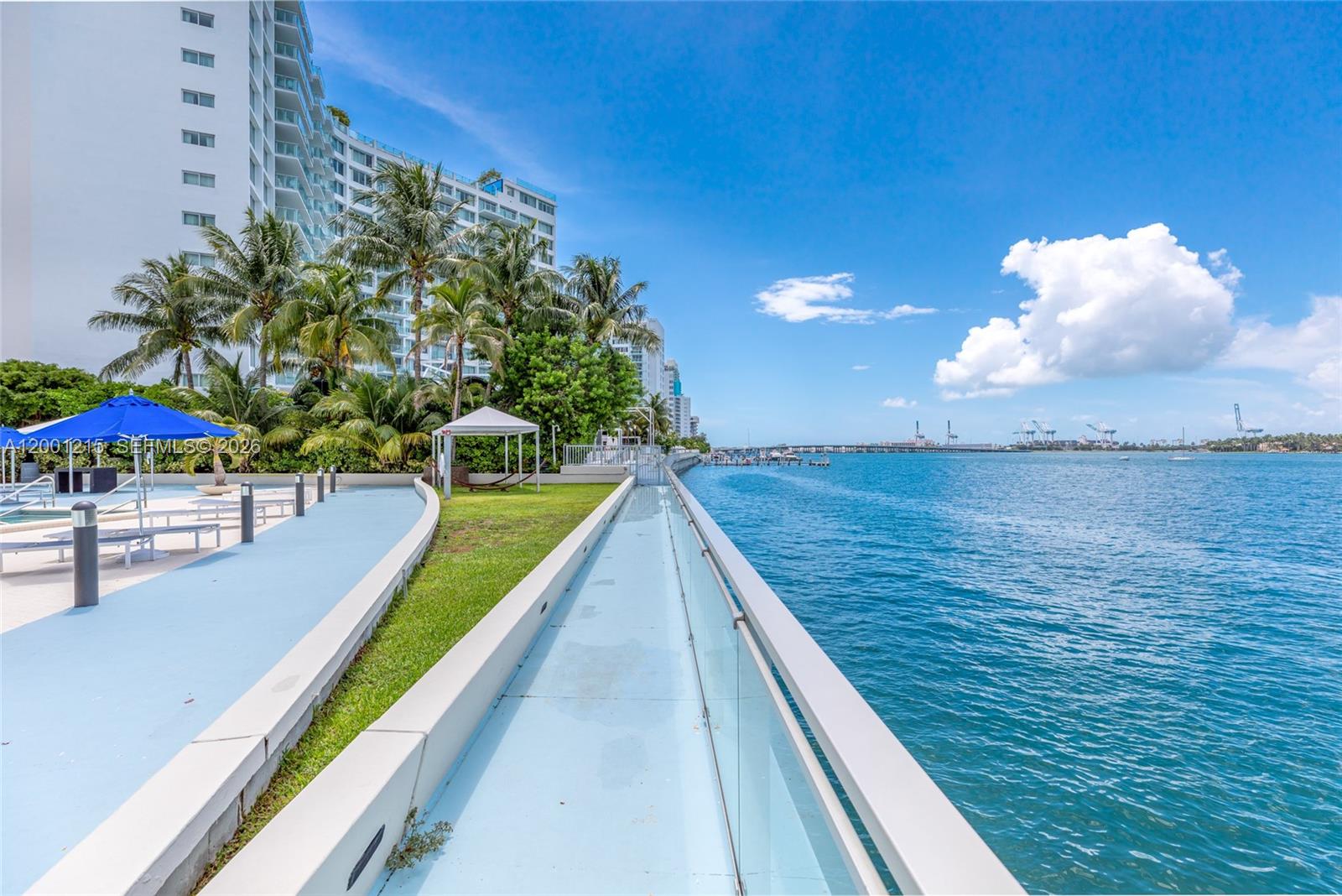 A paved walkway runs alongside a waterfront building with palm trees and a blue sky — 1200 West Ave, Miami Beach FL 33139, MIAMI BEACH, FL
