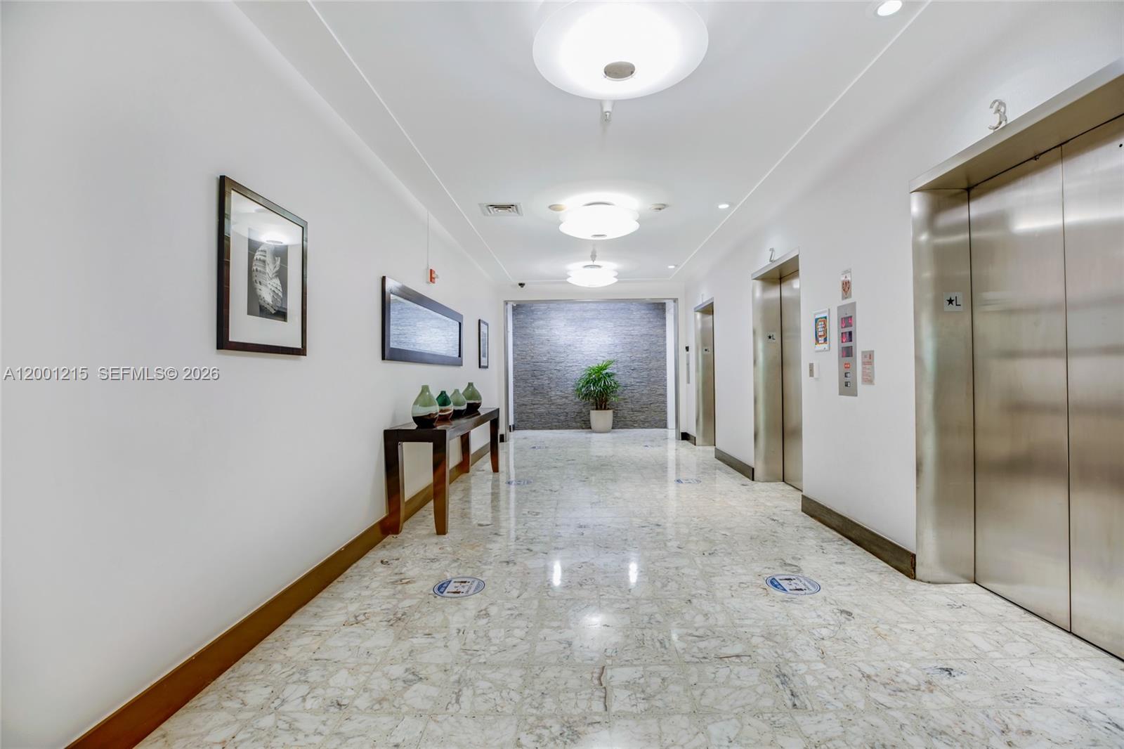 A hallway features marble floors, two elevators, a console table with vases, and recessed lighting — 1200 West Ave, Miami Beach FL 33139, MIAMI BEACH, FL