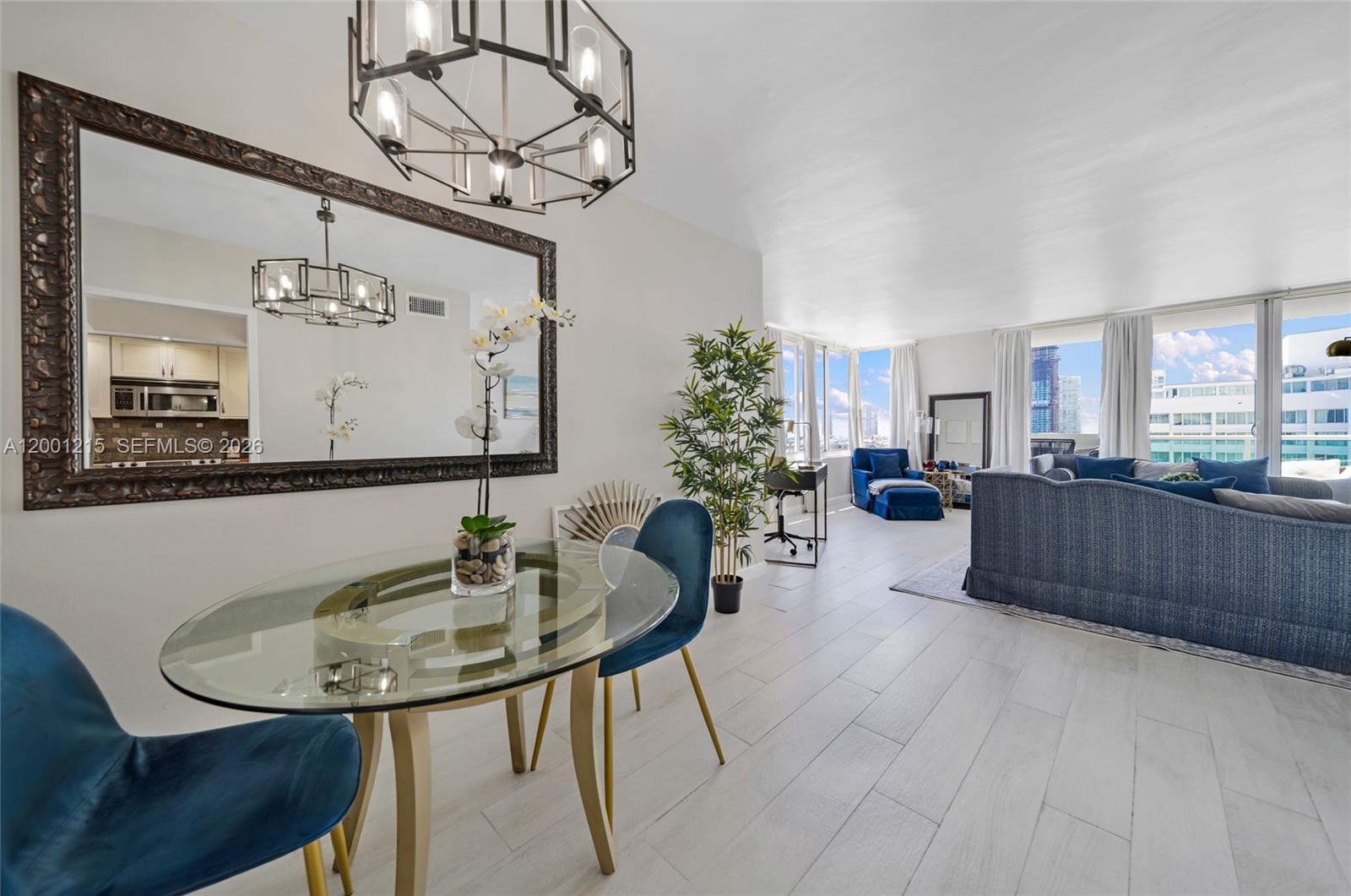 A dining area with a glass table and blue chairs overlooks a bright living room — 1200 West Ave, Miami Beach FL 33139, MIAMI BEACH, FL