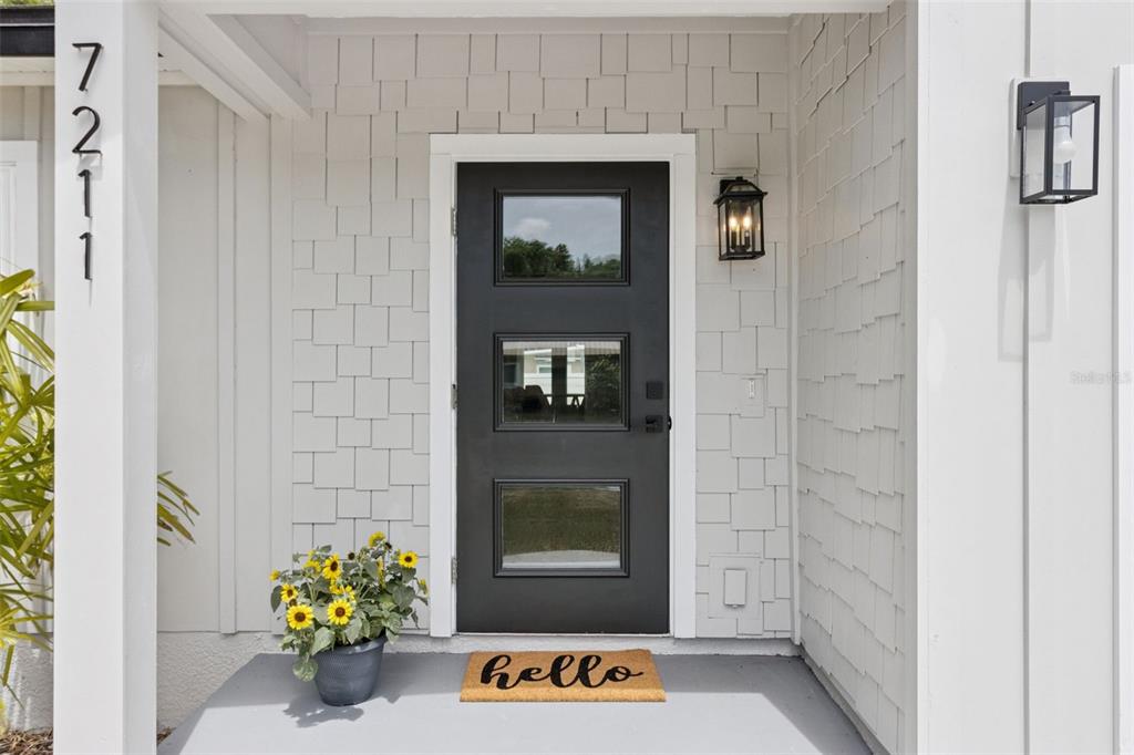 A black front door with three glass panels sits on a porch with shingled siding — 7211 ORPINE DRIVE N, ST PETERSBURG, FL