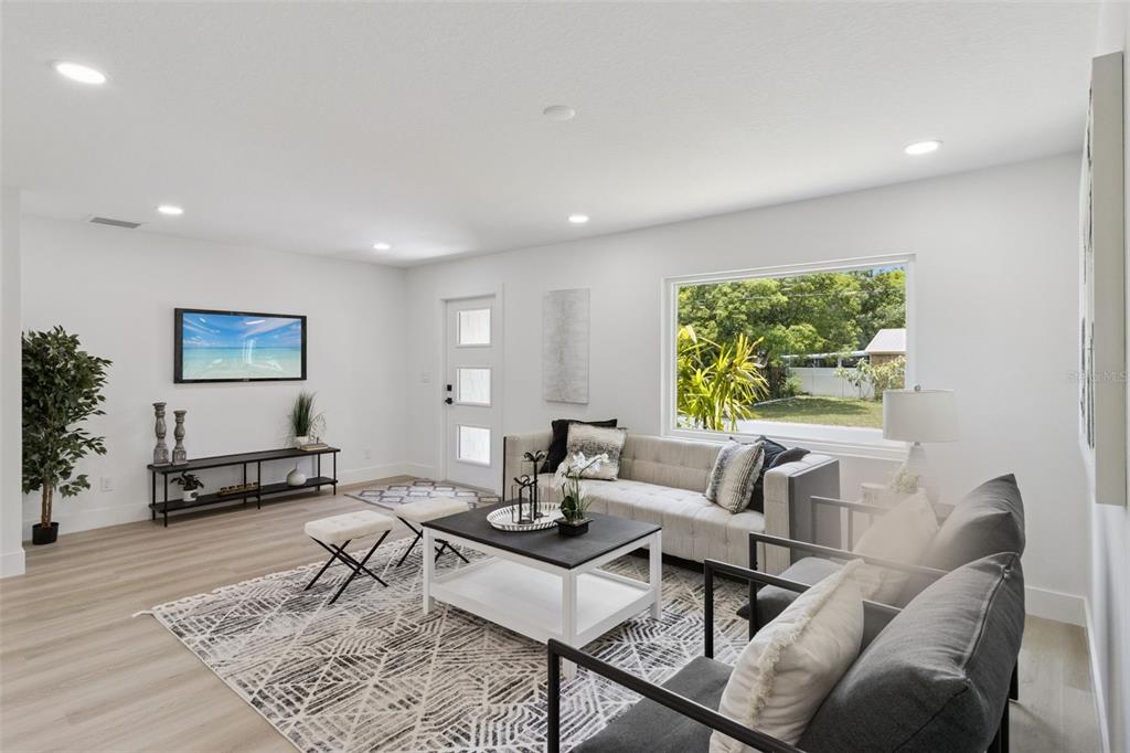 A bright living room features light wood floors, a patterned area rug, and modern furniture — 7211 ORPINE DRIVE N, ST PETERSBURG, FL