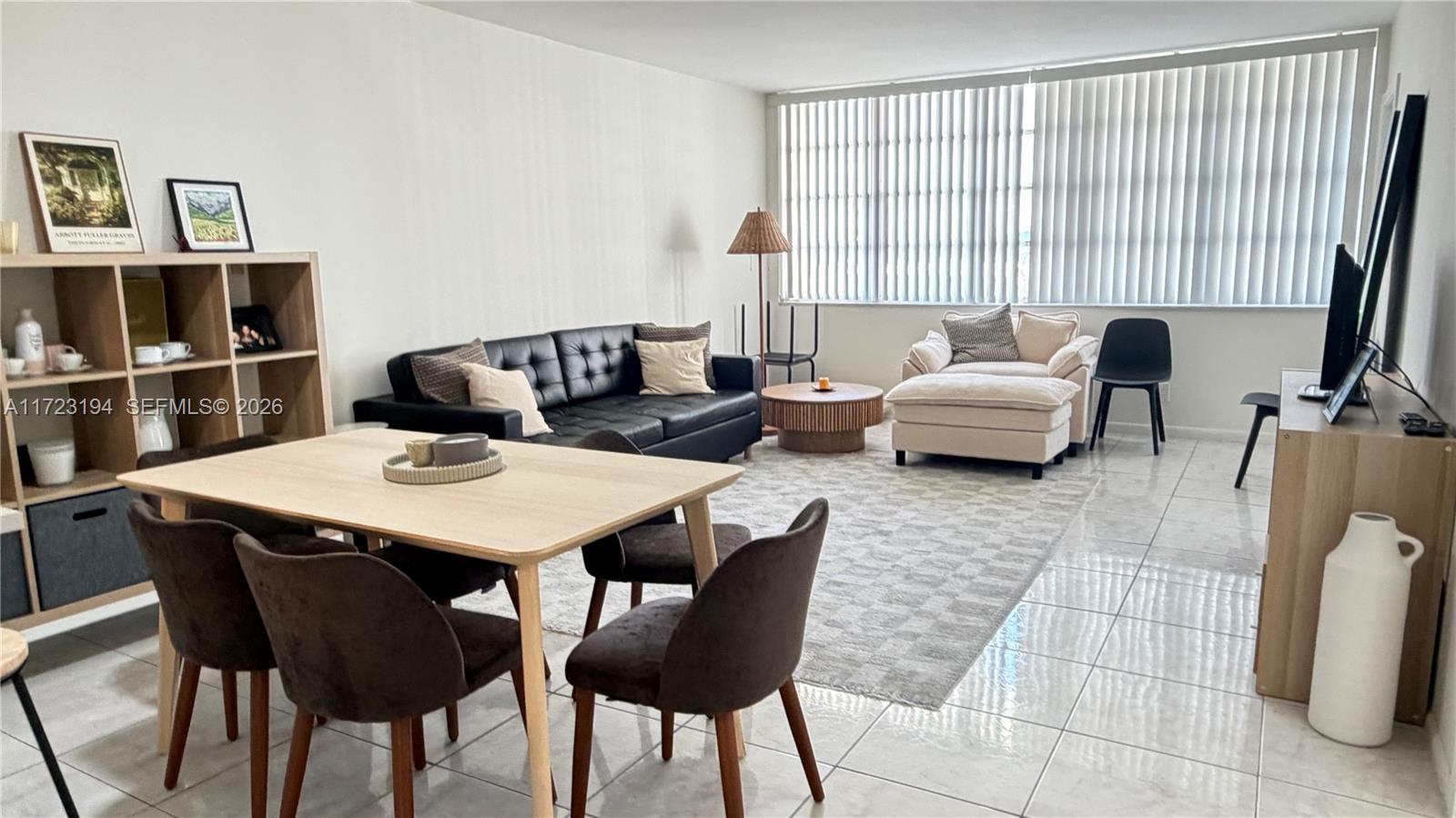This living and dining area features tile flooring, a black sofa, and a large window — 1825 S Ocean Dr # 506, Hallandale Beach FL 33009, HALLANDALE BEACH, FL