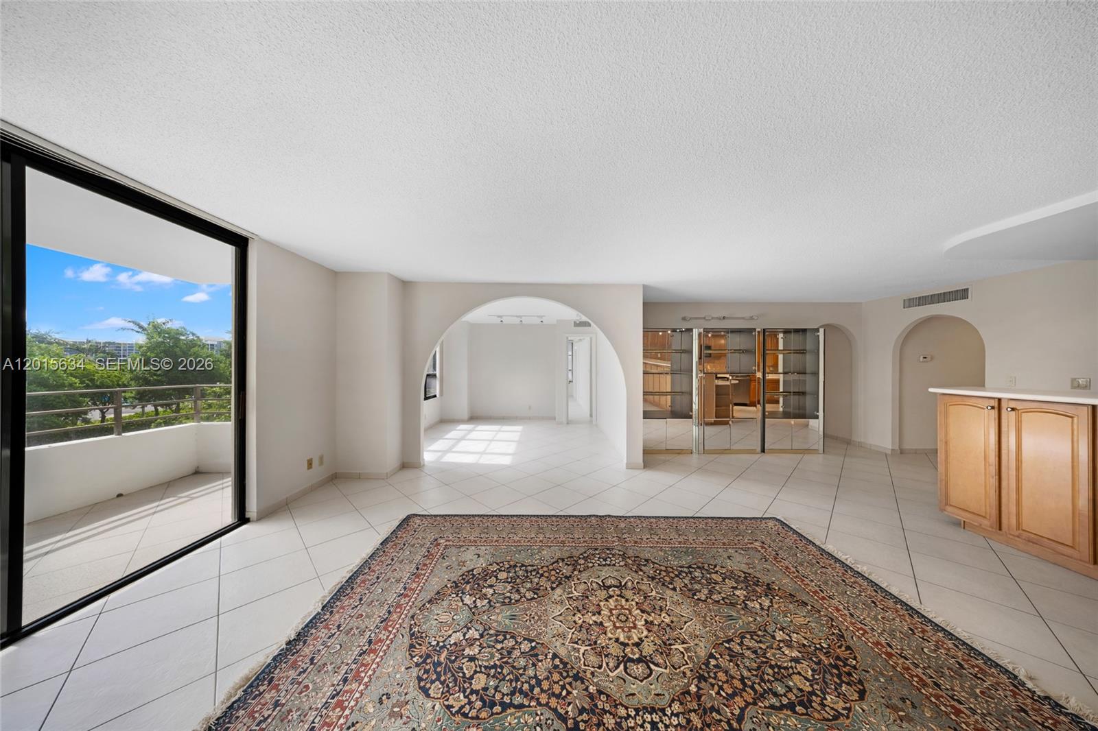 An open living area features a large rug, tiled floors, arched doorways, and a balcony — 600 Three Islands Blvd # 212, Hallandale Beach FL 33009, HALLANDALE BEACH, FL
