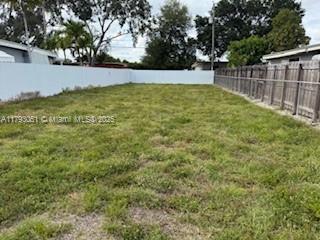 A flat, grassy vacant lot is enclosed by a white wall and a wooden fence — 137 W 32 ST, Hialeah FL 33012, HIALEAH, FL