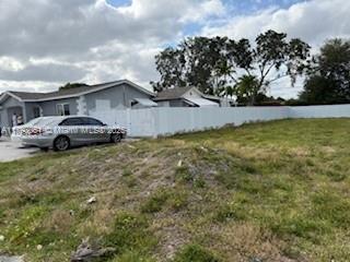 A gray house with a white fence stands next to a large, grassy vacant lot — 137 W 32 ST, Hialeah FL 33012, HIALEAH, FL