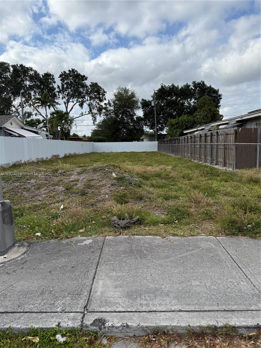 An empty residential lot is enclosed by white and wooden fences under a cloudy sky — 137 W 32 ST, Hialeah FL 33012, HIALEAH, FL