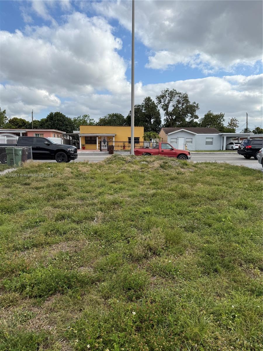 A vacant grassy lot sits in front of a street with houses and parked vehicles — 137 W 32 ST, Hialeah FL 33012, HIALEAH, FL