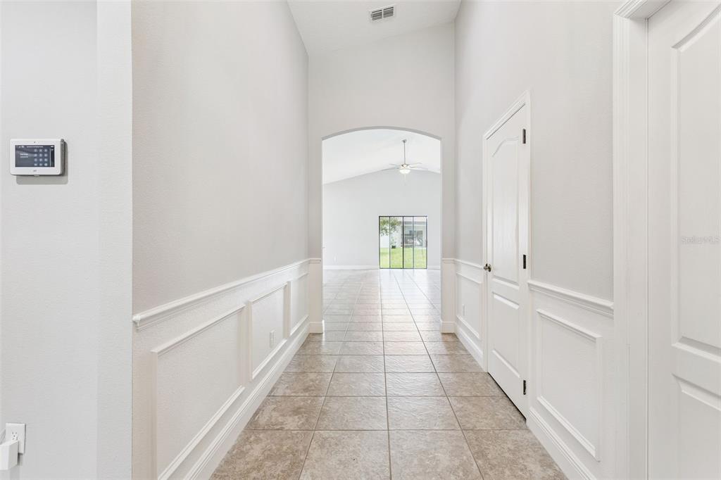 A tiled hallway with white wainscoting leads to an open living area with a ceiling fan — 1144 CAMBOURNE DR, KISSIMMEE, FL