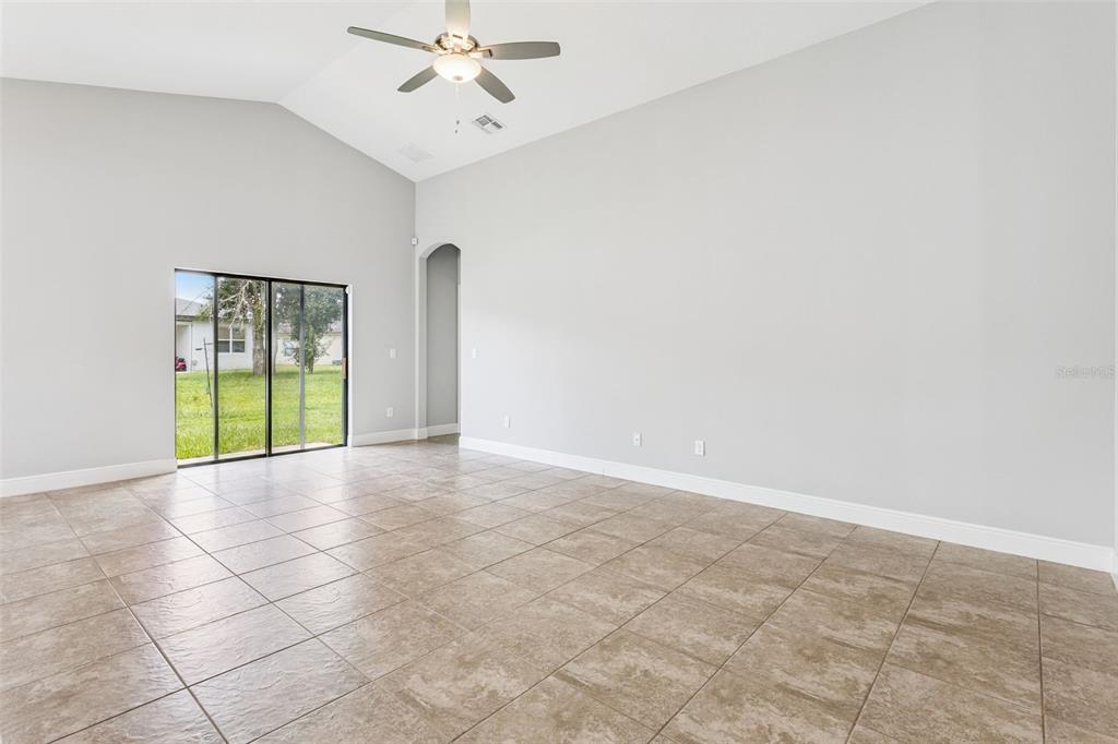An empty room with light-colored walls, tiled floors, a vaulted ceiling, and sliding glass doors — 1144 CAMBOURNE DR, KISSIMMEE, FL