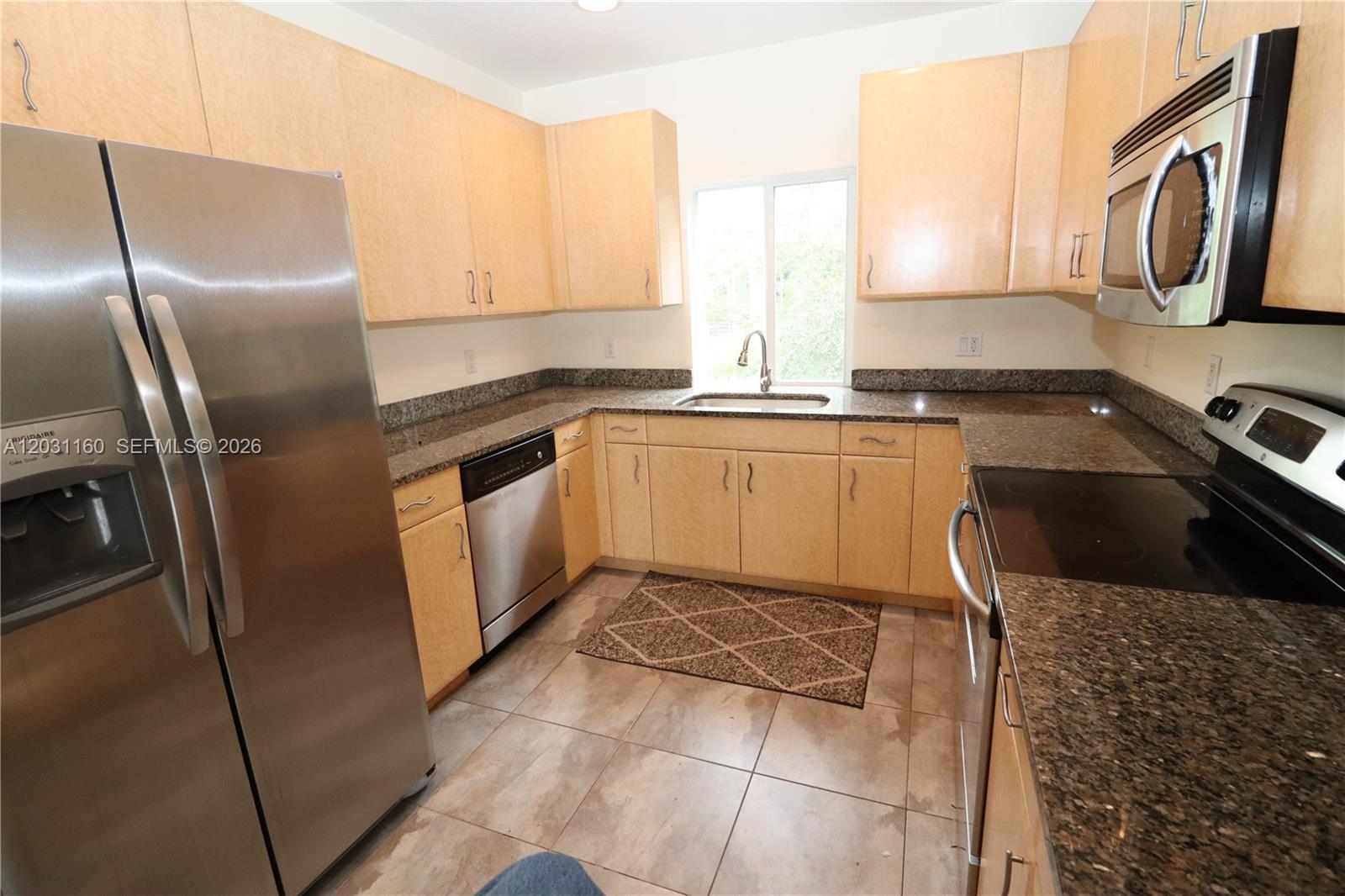 A kitchen features light wood cabinets, granite countertops, stainless steel appliances, and tile flooring — 609 NE 28th St # 1, Wilton Manors FL 33334, WILTON MANORS, FL