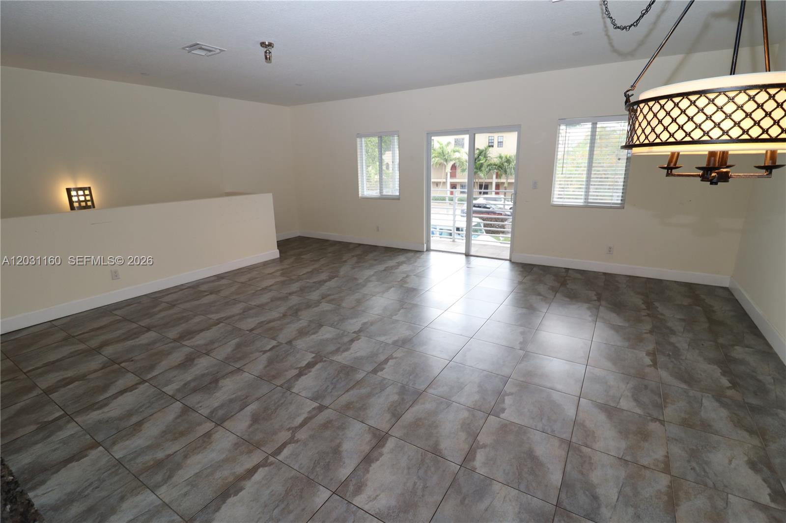 An empty room features large gray tile flooring, a decorative chandelier, and sliding glass doors — 609 NE 28th St # 1, Wilton Manors FL 33334, WILTON MANORS, FL