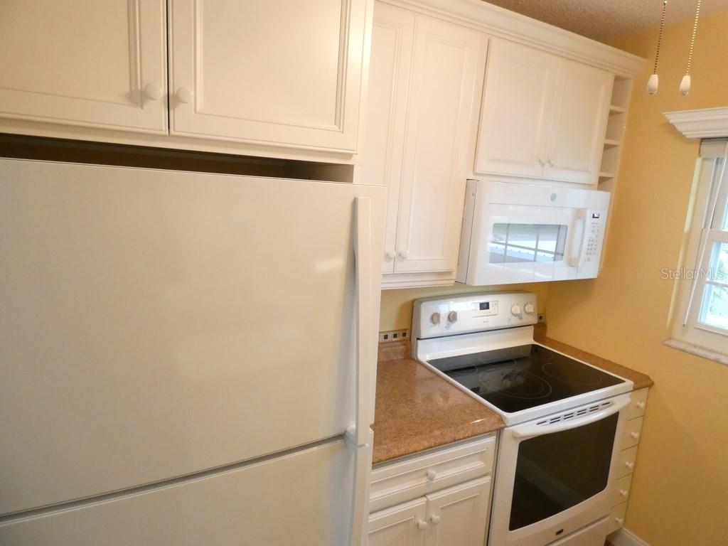 A kitchen features white cabinets, a double-basin sink, and tan countertops against yellow walls — 4801 AIRPORT ROAD UNIT 213, ZEPHYRHILLS, FL