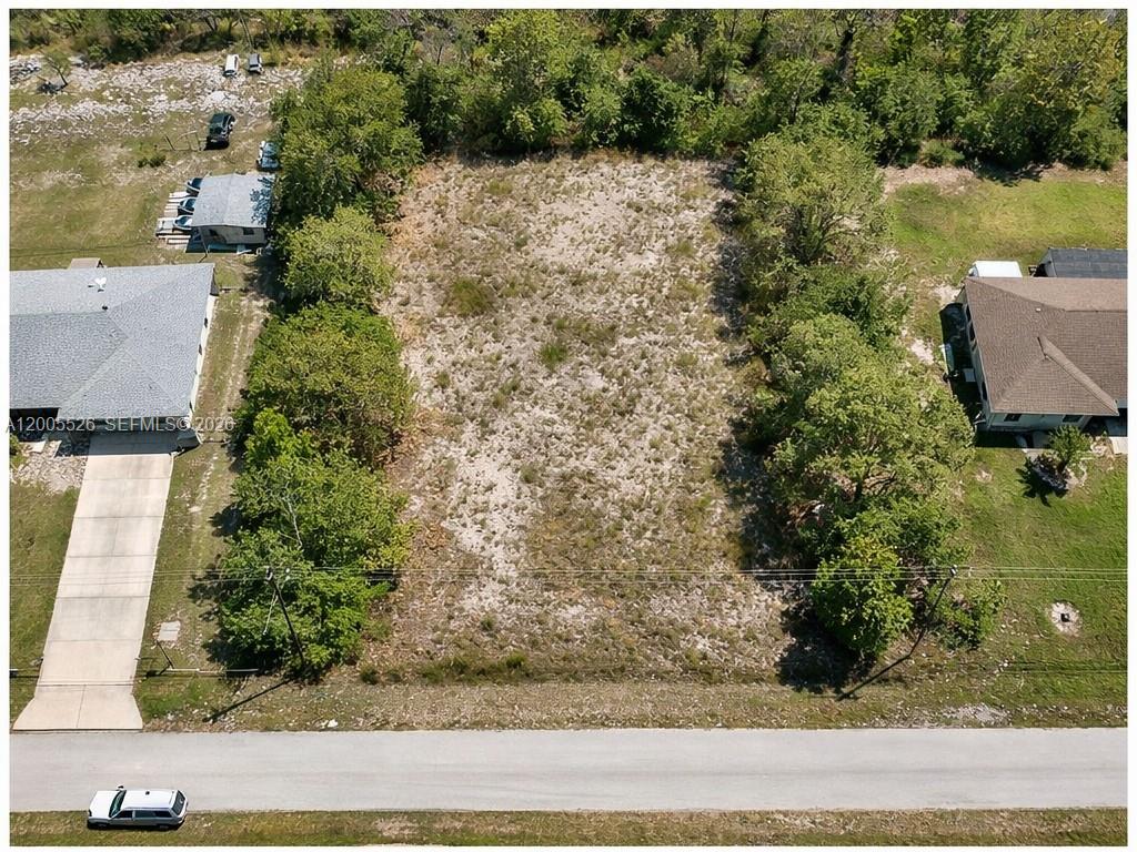 An aerial view shows a vacant, rectangular residential lot bordered by trees and neighboring houses — 682 Woodcrest Dr, Lehigh Acres FL 33972, LEHIGH ACRES, FL