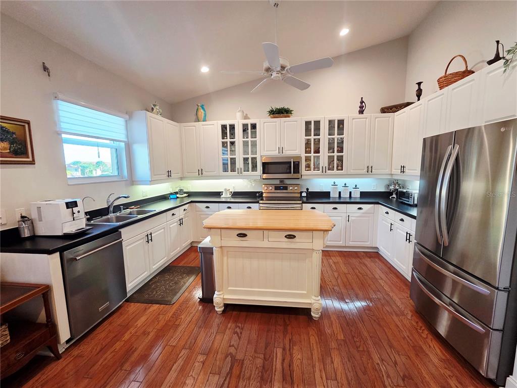 A kitchen features white cabinets, stainless steel appliances, a wooden island, and hardwood flooring — 6775 HUNTINGTON LAKES CIRCLE UNIT 202, NAPLES, FL
