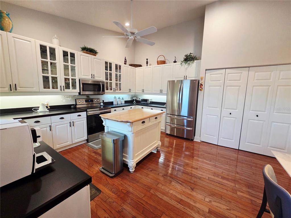 A kitchen features white cabinetry, a wooden island, stainless steel appliances, and hardwood flooring — 6775 HUNTINGTON LAKES CIRCLE UNIT 202, NAPLES, FL
