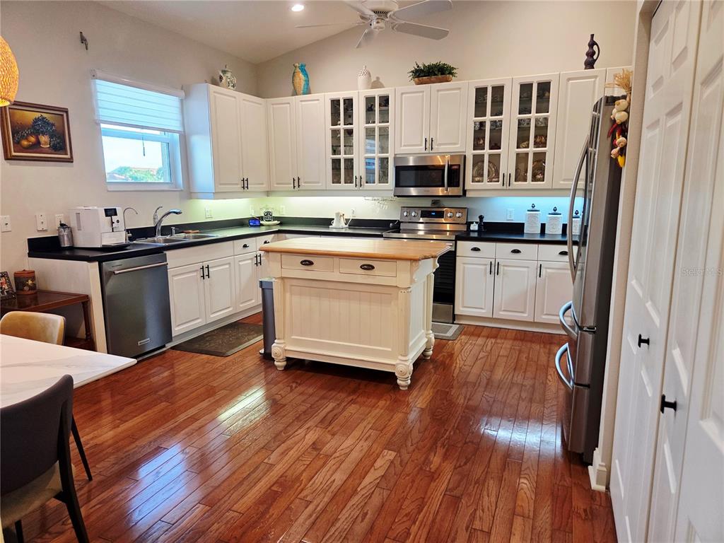 A kitchen features white cabinets, a wooden island, stainless steel appliances, and hardwood flooring — 6775 HUNTINGTON LAKES CIRCLE UNIT 202, NAPLES, FL