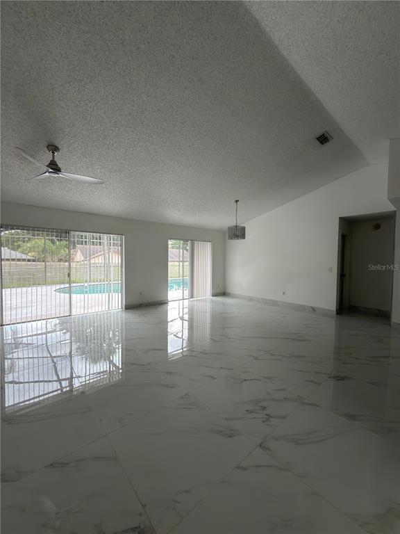 A spacious living room features white marble-look tile floors, vaulted ceilings, and sliding glass doors — 9142 SABAL PALM CIRCLE, WINDERMERE, FL