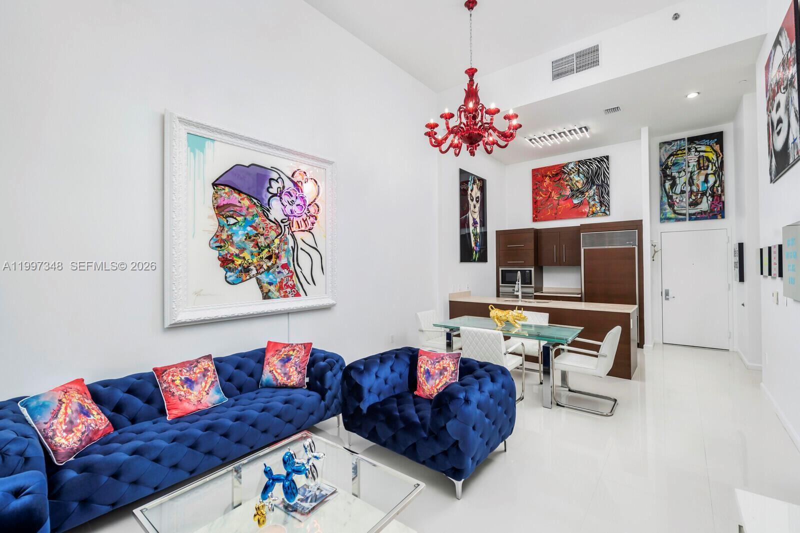 A modern living and dining area features a blue tufted sofa, red chandelier, and artwork — 475 Brickell Ave # 2811, Miami FL 33131, MIAMI, FL