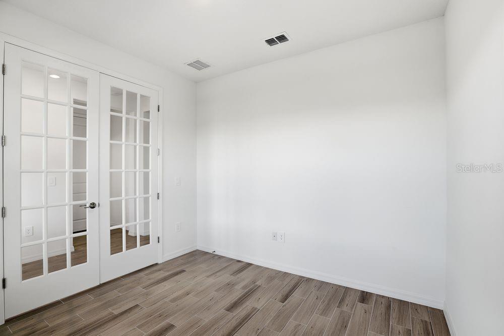 An empty room with white walls, wood-look tile flooring, and white French doors — 14788 FIELD DAISY DRIVE, WINTER GARDEN, FL
