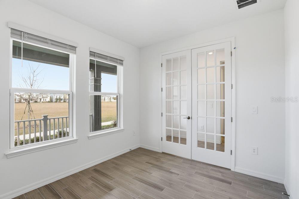 A room with white walls, wood-look tile flooring, two windows, and white French doors — 14788 FIELD DAISY DRIVE, WINTER GARDEN, FL