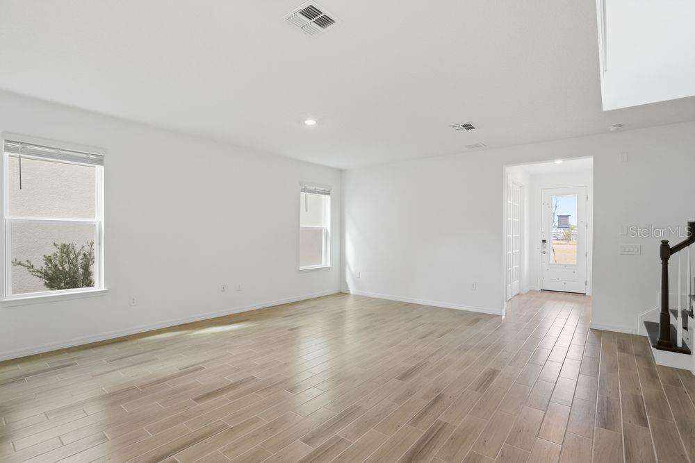 An empty living room features light wood-look tile flooring, white walls, and a front entrance — 14788 FIELD DAISY DRIVE, WINTER GARDEN, FL