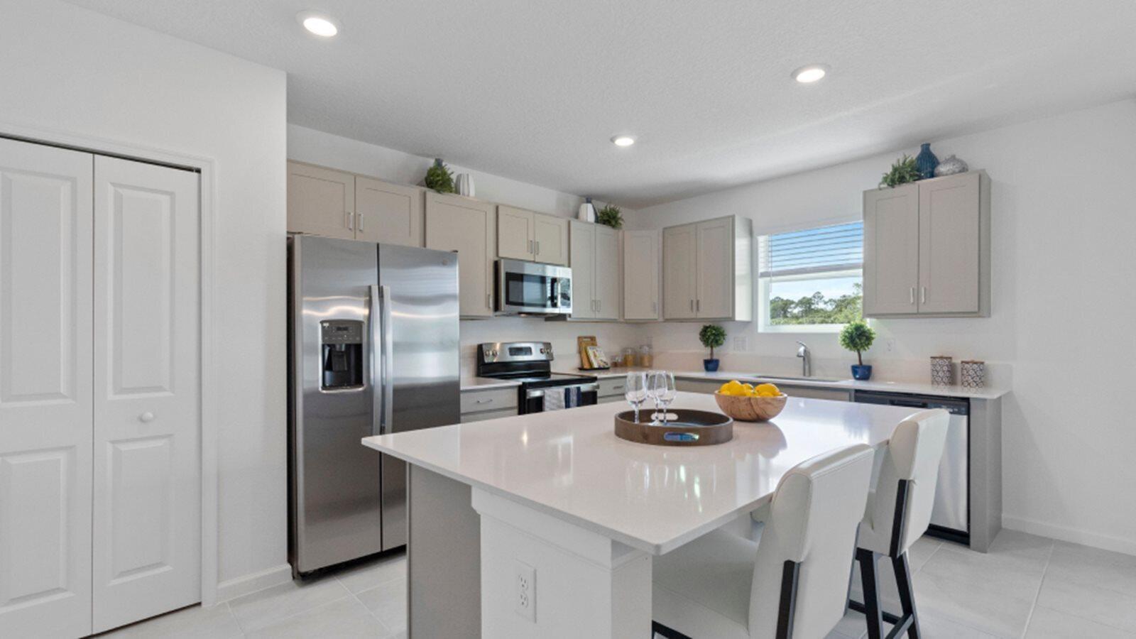 A modern kitchen features light gray cabinets, stainless steel appliances, and a white quartz island — 3202 Spanish Cedar Place, Fort Pierce FL 34946, FORT PIERCE, FL