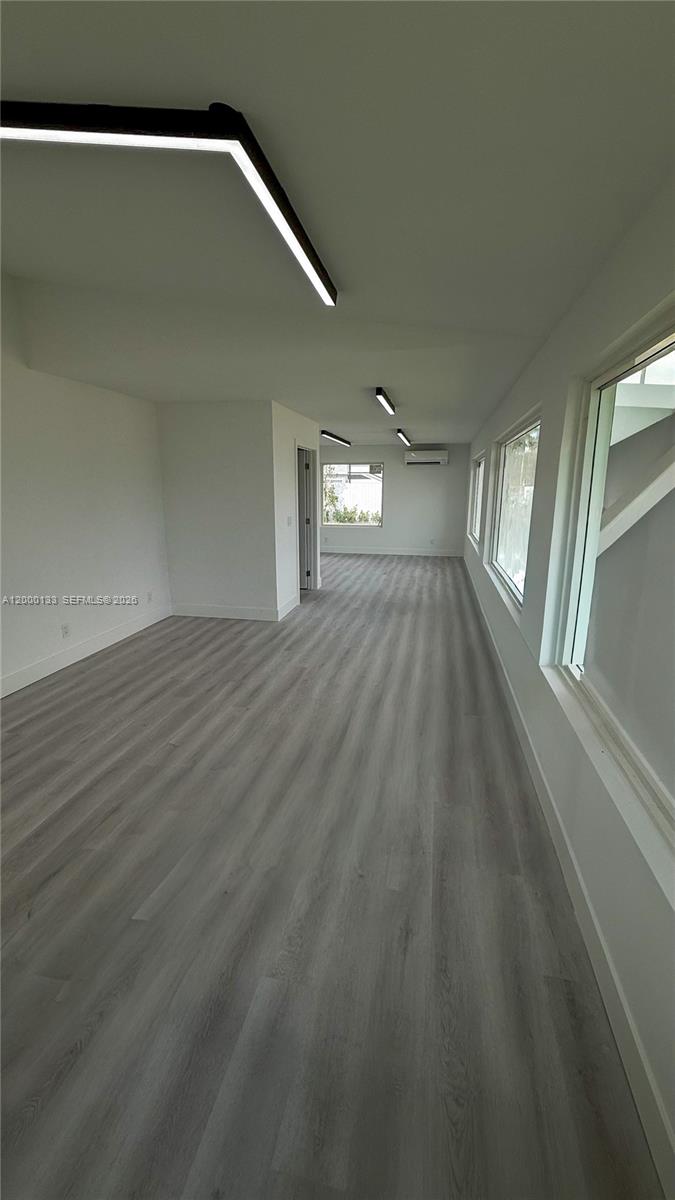 An empty room features light gray wood-look flooring, white walls, and modern linear ceiling lights — 7061 Taft St # C, Hollywood FL 33024, HOLLYWOOD, FL