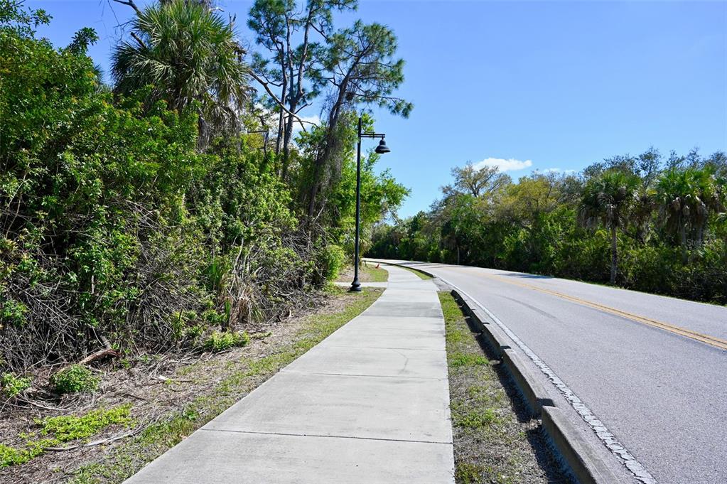 A concrete sidewalk runs alongside a paved road bordered by dense trees and vegetation — 22901 BAYSHORE ROAD, PUNTA GORDA, FL